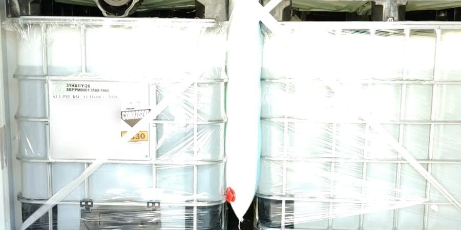 IBCs of industrial chemical with corrosive labels, stretch-wrapped and braced inside a shipping container