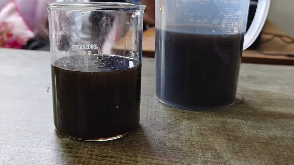 Sample of LABSA 90% in a glass beaker beside a measuring jug of the same dark brown liquid