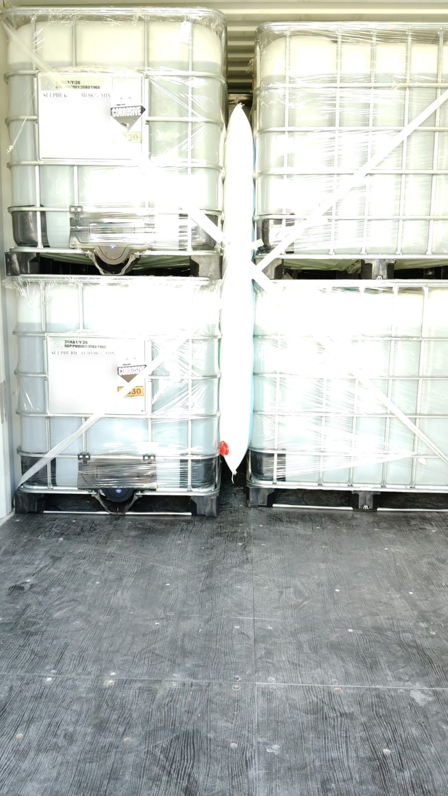 Stretch-wrapped sulphuric acid IBCs with corrosive and UN 1830 labels secured inside a shipping container